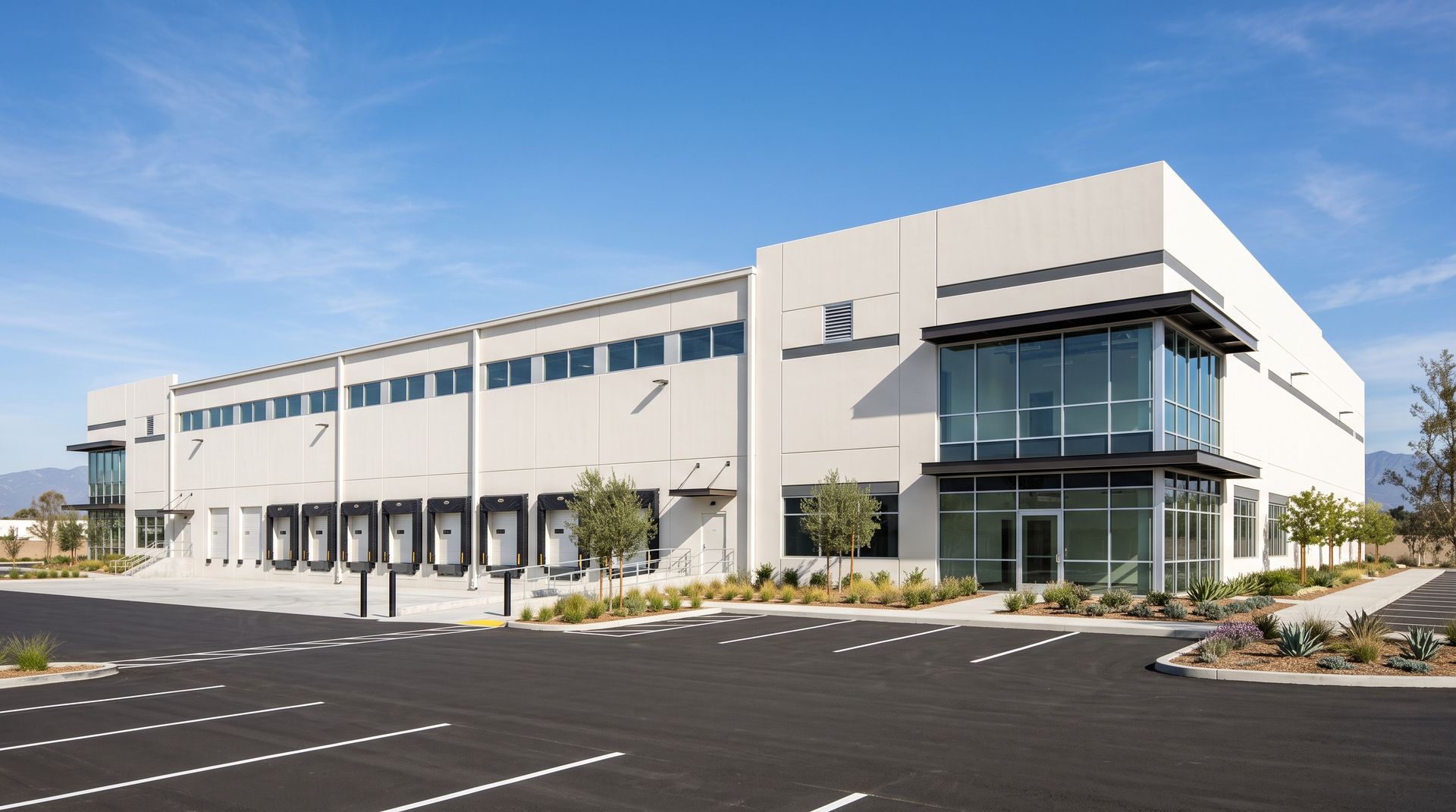 Photorealistic render of a white concrete tilt-up industrial logistics building with a two-storey glass office corner and a row of dock-high loading doors